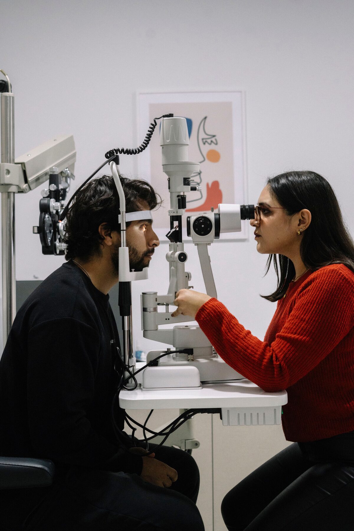 A clinician examines a seated patient's eye with a slit lamp.